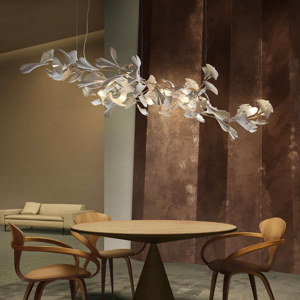 The Clérachic gingko linear chandelier lit above a round table with sculptural wooden chairs.