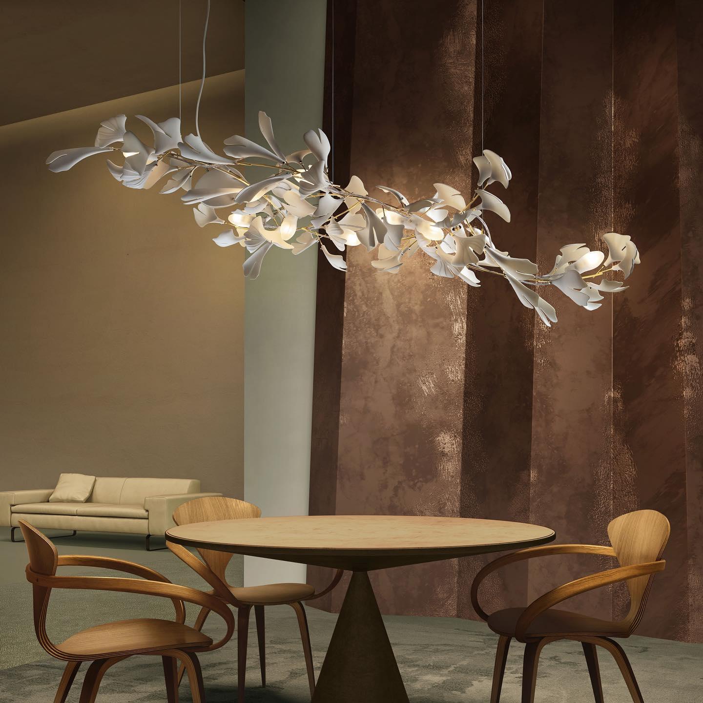 The Clérachic gingko linear chandelier lit above a round table with sculptural wooden chairs.