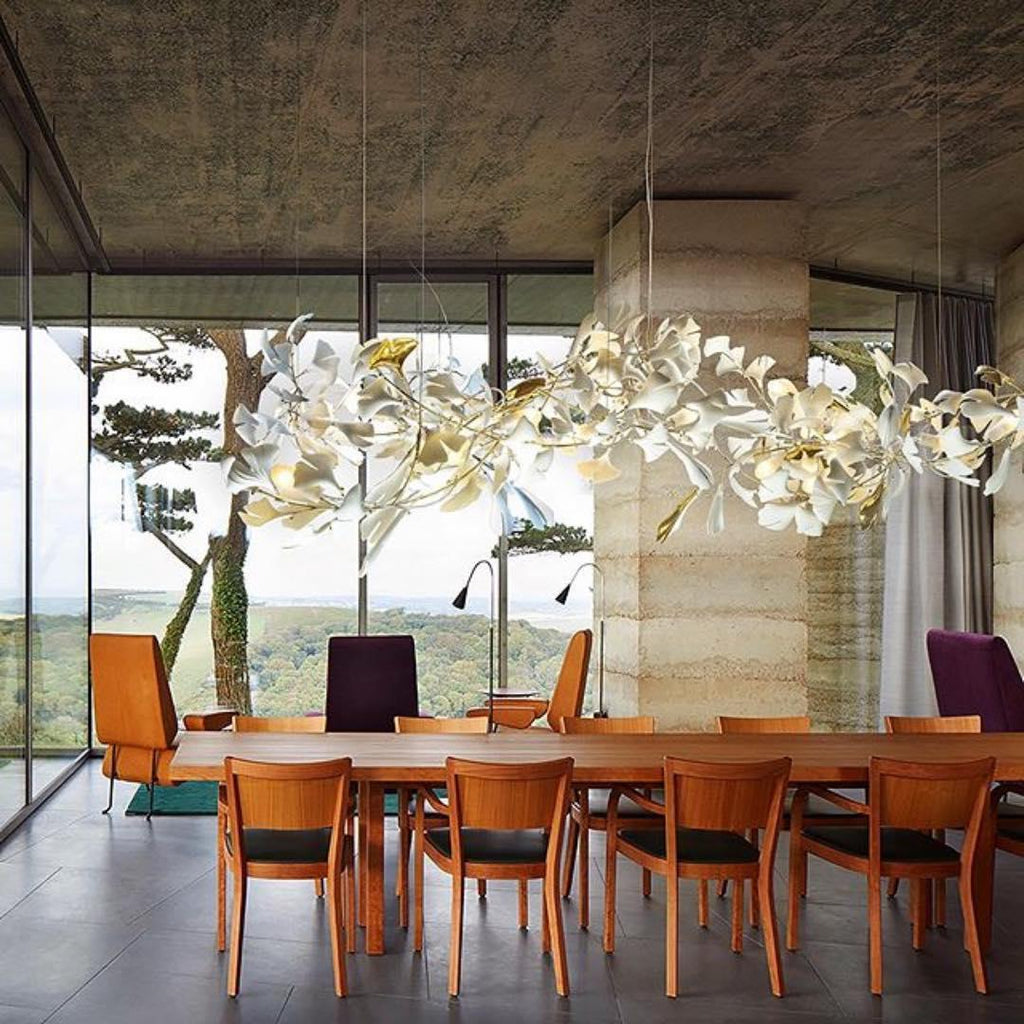 The Clérachic gingko linear chandelier lit above a long dining table in a glass-walled room.