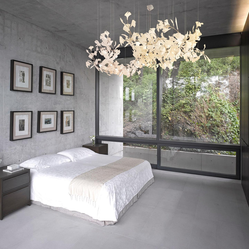 The Clérachic gingko linear chandelier lit above a bed in a concrete room with a forest view.