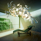 Clérachic gingko linear chandelier lit in a concrete room with a lounge chair and green courtyard.