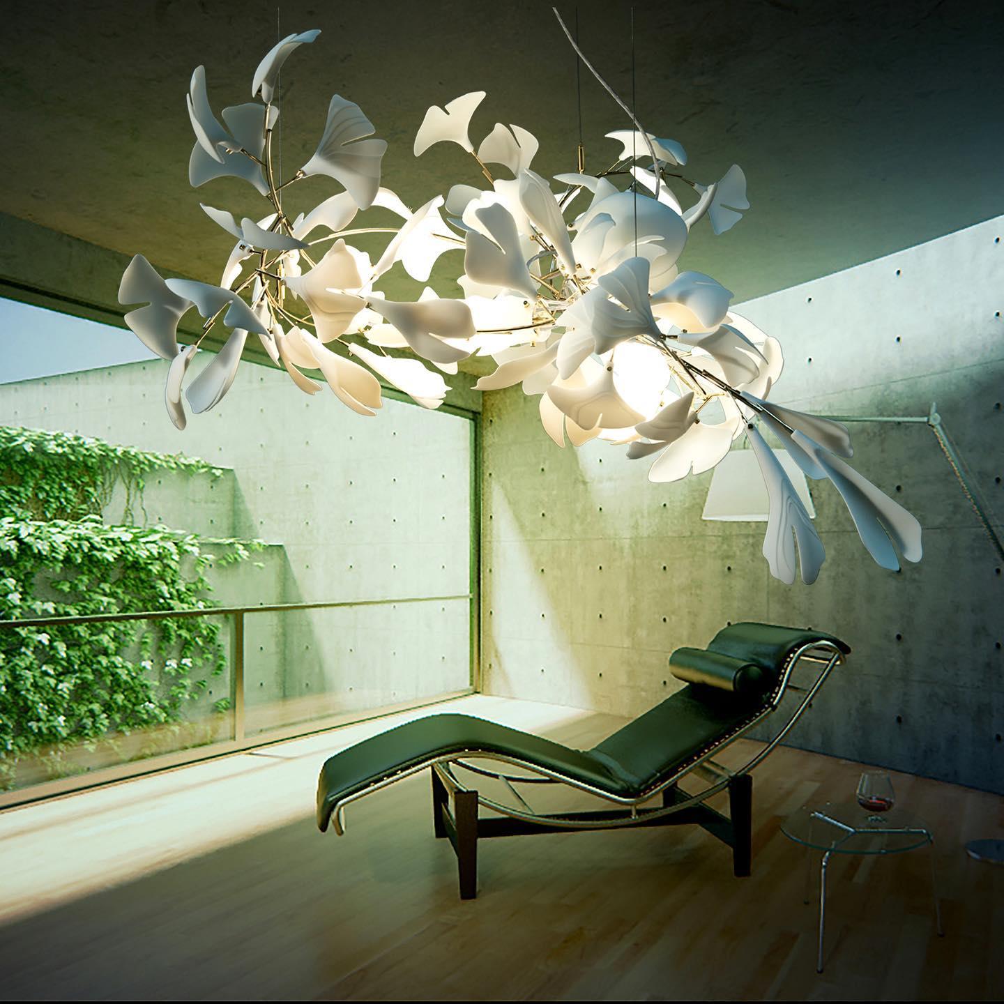 Clérachic gingko linear chandelier lit in a concrete room with a lounge chair and green courtyard.