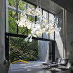 The Clérachic gingko linear chandelier lit beside tall windows in a concrete-walled living space.