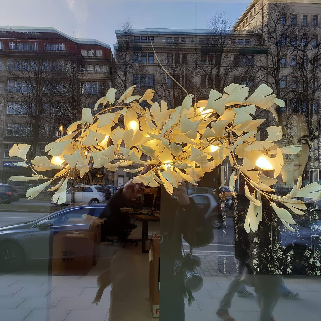 The Clérachic gingko chandelier lit in a street-facing window, ceramic leaves glowing above passers-by.