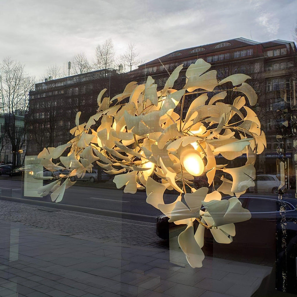 Clérachic gingko chandelier lit in a shopfront window against a city street at dusk.
