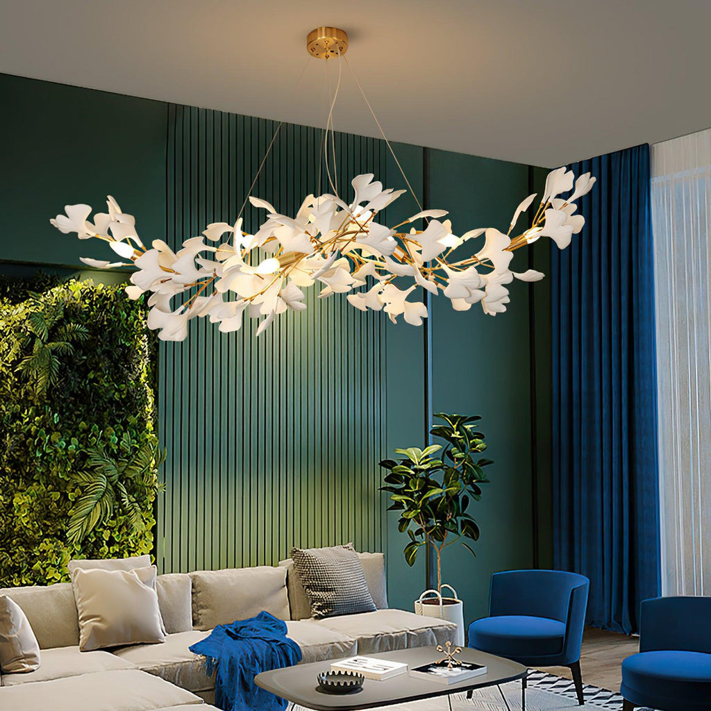 The Clérachic gingko chandelier lit above a pale sofa against a green wall and living plant screen.