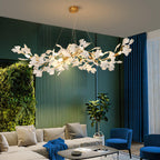 The Clérachic gingko chandelier lit above a pale sofa against a green wall and living plant screen.