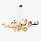 Clérachic gingko chandelier on white, ceramic leaves scattered along gold branches beneath a round canopy.