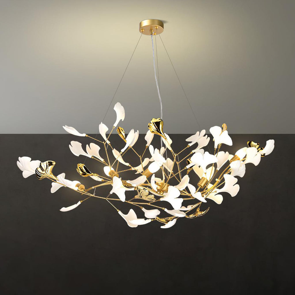 The Clérachic gingko chandelier lit against a dark wall, its leaves glowing warm along gilded stems.