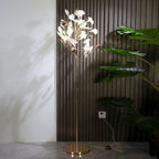 Clérachic gingko floor lamp lit beside dark slatted panelling and a large leafy plant.