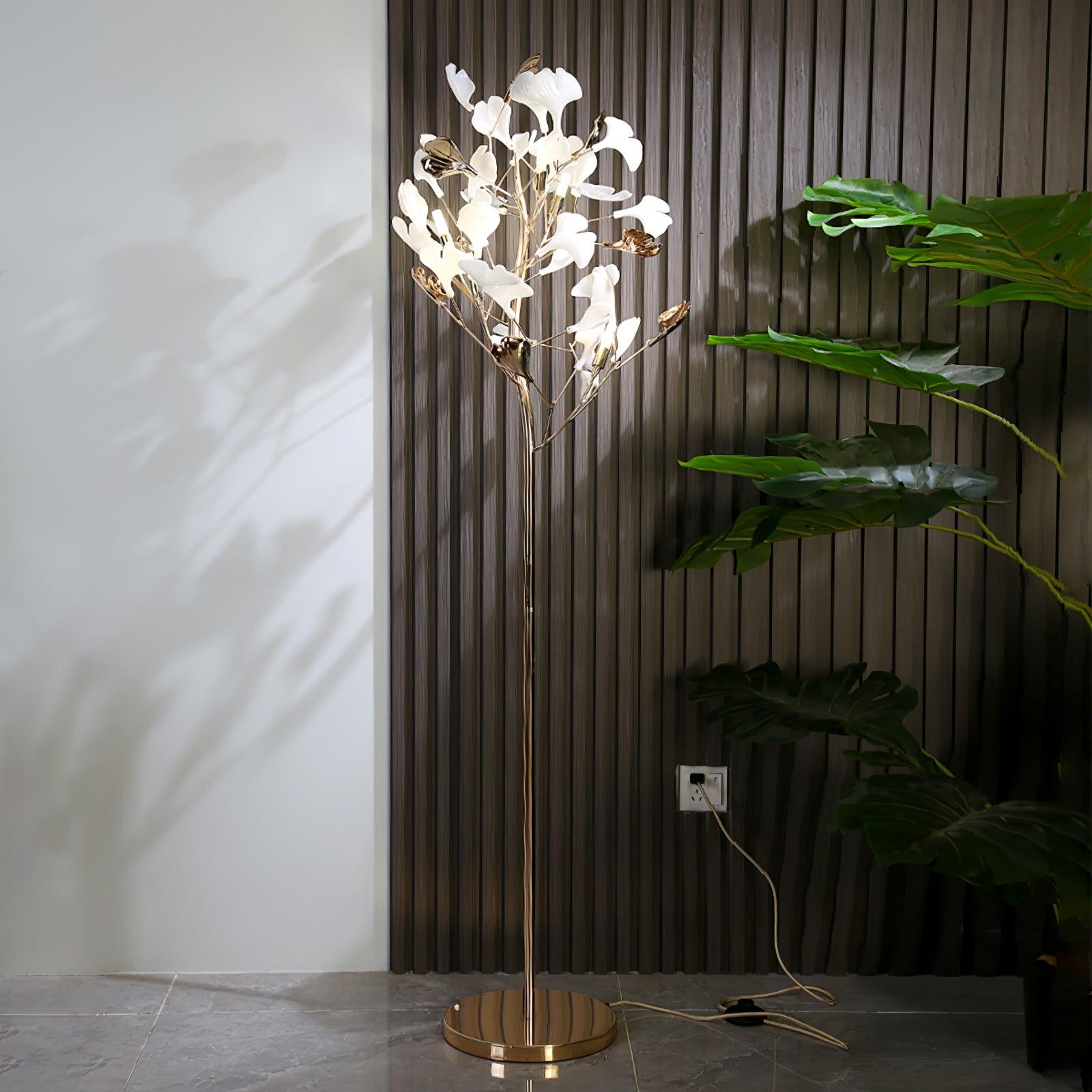 Clérachic gingko floor lamp lit beside dark slatted panelling and a large leafy plant.