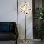 The Clérachic gingko floor lamp lit next to a brown leather sofa with a blue cushion.