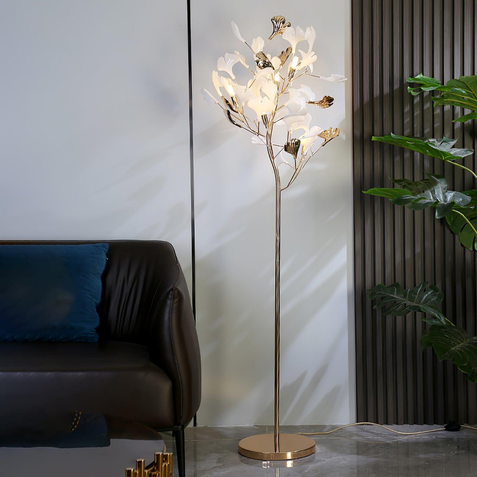 The Clérachic gingko floor lamp lit next to a brown leather sofa with a blue cushion.