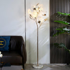 Clérachic gingko floor lamp glowing beside a leather sofa, its ceramic leaves catching the light.