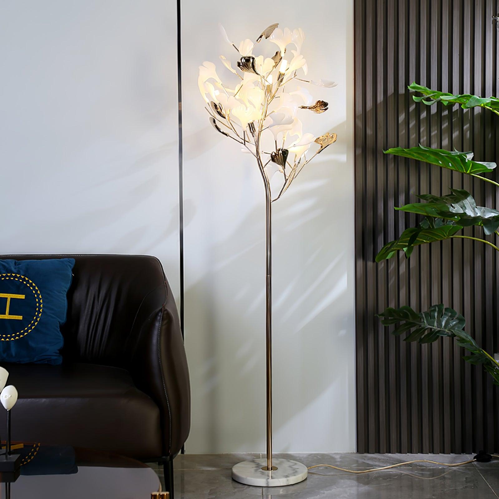 Clérachic gingko floor lamp glowing beside a leather sofa, its ceramic leaves catching the light.
