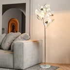 The Clérachic gingko floor lamp lit beside a grey sofa in a warm-toned living room.