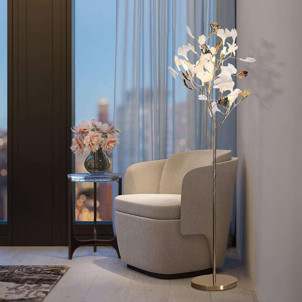 Clérachic gingko floor lamp lit by a window with a cream armchair and a vase of roses.