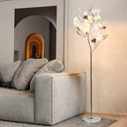 The Clérachic gingko floor lamp on a marble base beside a deep grey sofa and arched wall niche.