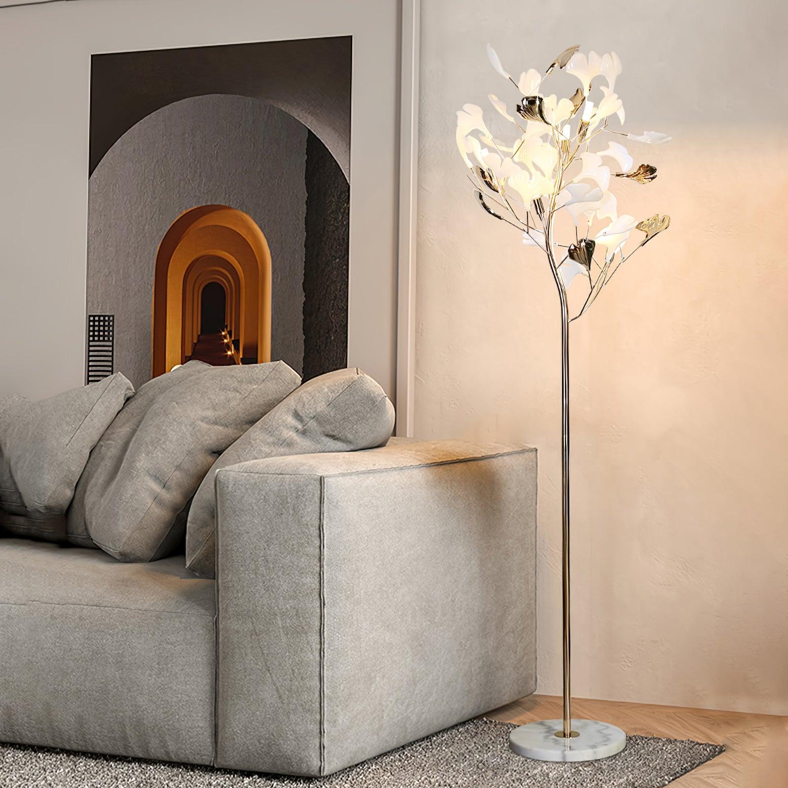 The Clérachic gingko floor lamp on a marble base beside a deep grey sofa and arched wall niche.