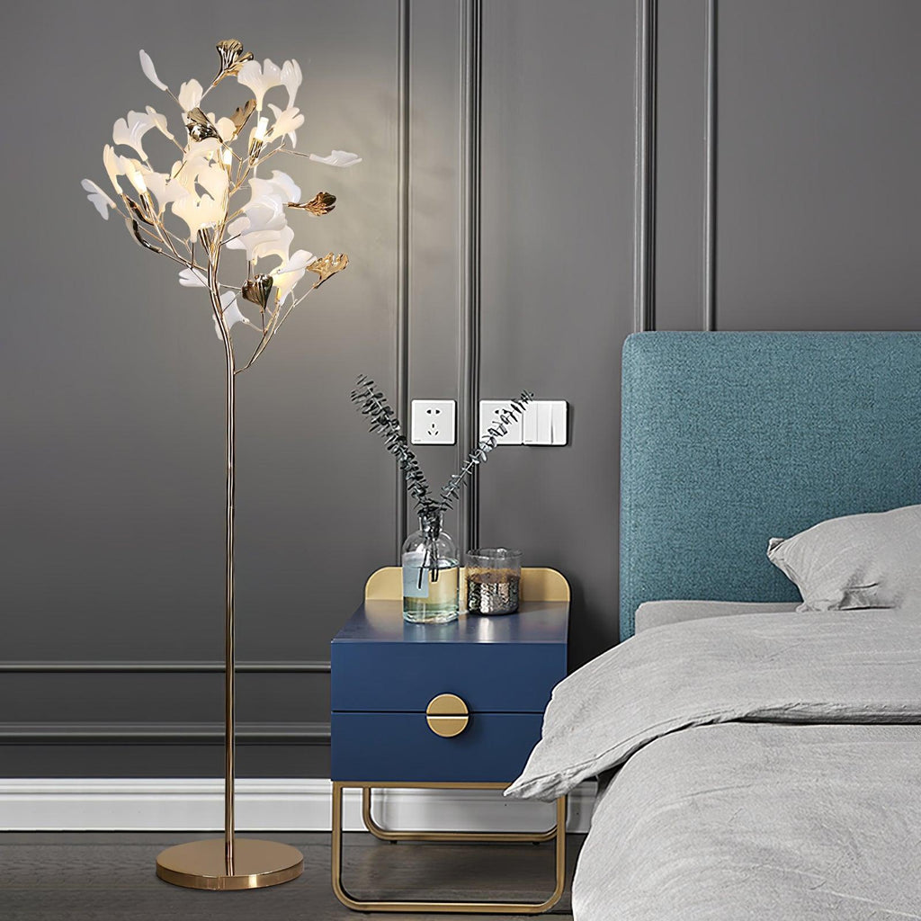 Clérachic gingko floor lamp lit beside a bed with a teal headboard and a blue bedside cabinet.