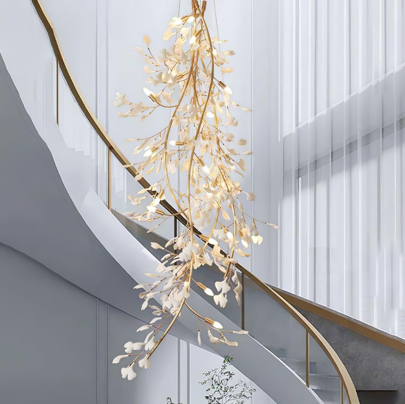 The Clérachic gingko cascade chandelier hanging beside a curved staircase in a bright double-height hall.