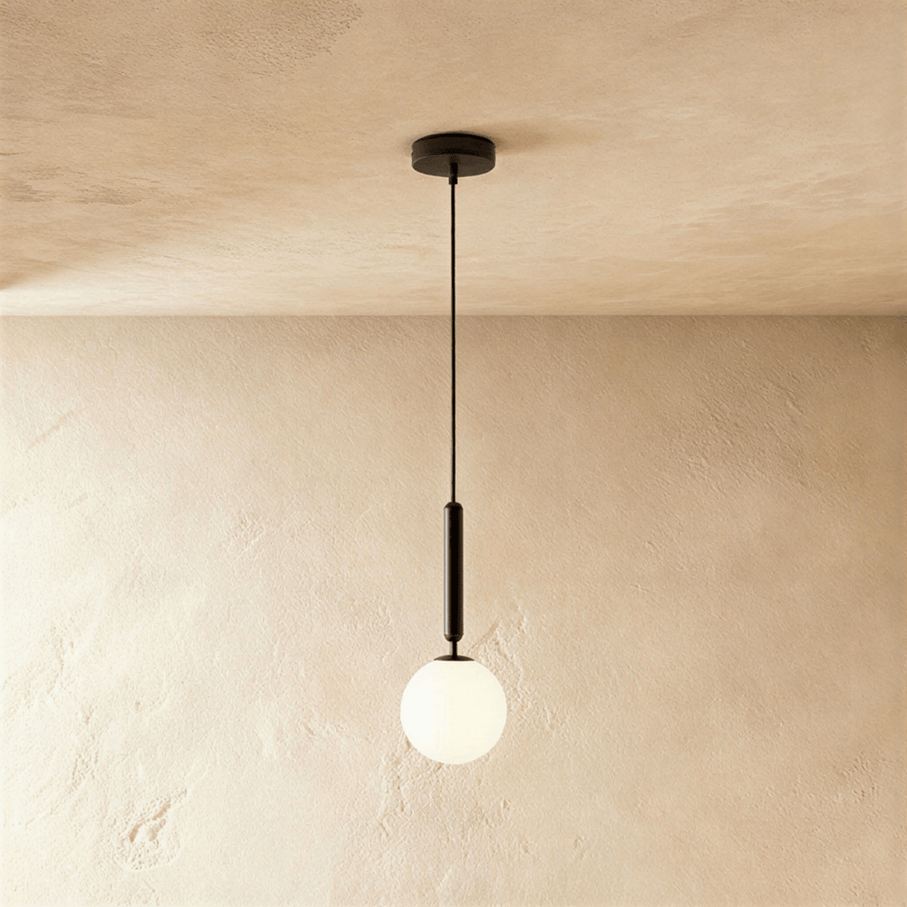 Clérachic single pendant with a milk white glass globe on a slim black rod and cord, hung against a limewashed wall.