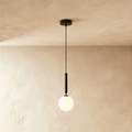 Clérachic single pendant with a milk white glass globe on a slim black rod and cord, hung against a limewashed wall.