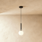 Clérachic single pendant with a milk white glass globe on a slim black rod and cord, hung against a limewashed wall.