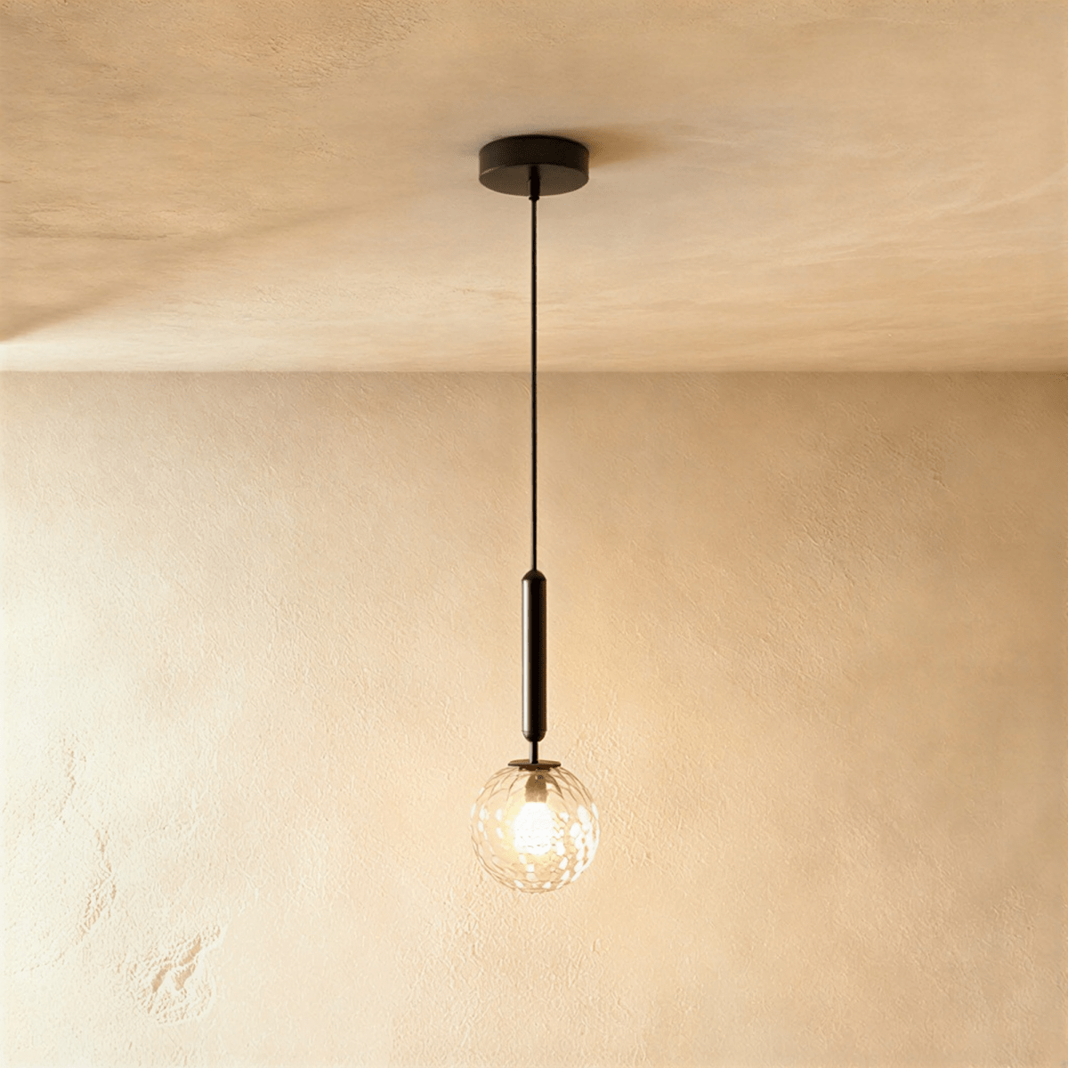 Clérachic single pendant with a clear textured glass globe and a lit bulb, on a black rod, against a warm plaster wall.