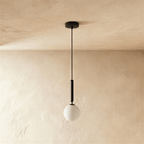 Clérachic single pendant, a milk white glass globe below a slim black cylinder and cord, on a plaster-toned wall.