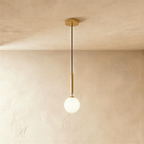 Clérachic single pendant with a milk white glass globe on a brushed gold rod and canopy, against a limewashed wall.