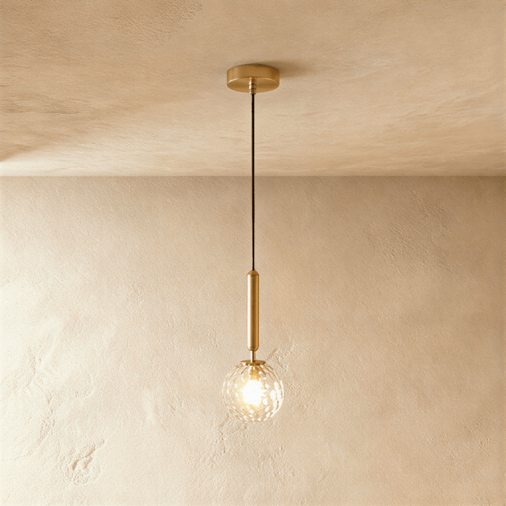 Clérachic single pendant with a clear faceted glass globe glowing on a brushed gold rod and round gold ceiling plate.