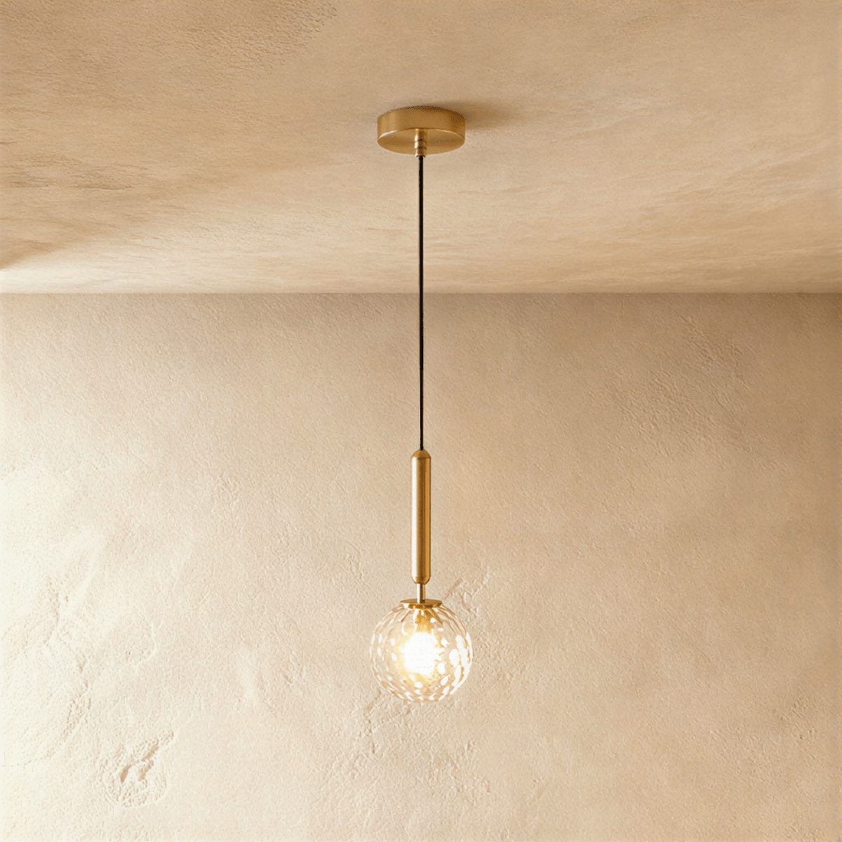 Clérachic single pendant with a clear faceted glass globe glowing on a brushed gold rod and round gold ceiling plate.