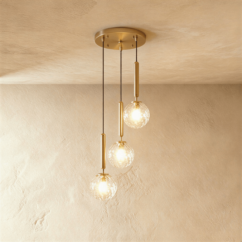 Clérachic three-head pendant on a round gold canopy, with clear faceted globes glowing at three staggered heights.