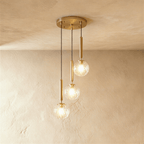 Clérachic three-head pendant on a round gold canopy, with clear faceted globes glowing at three staggered heights.