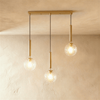Clérachic three-head linear pendant on a gold bar, with clear faceted glass globes lit at three staggered heights.