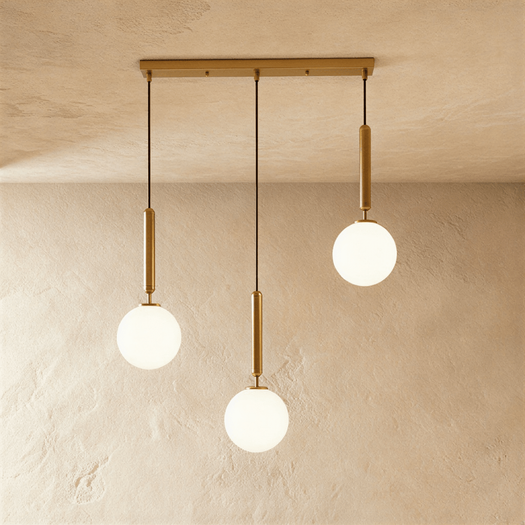 Clérachic three-head linear pendant on a gold bar, with milk white glass globes hung at three different heights.