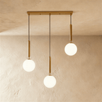Clérachic three-head linear pendant on a gold bar, with milk white glass globes hung at three different heights.