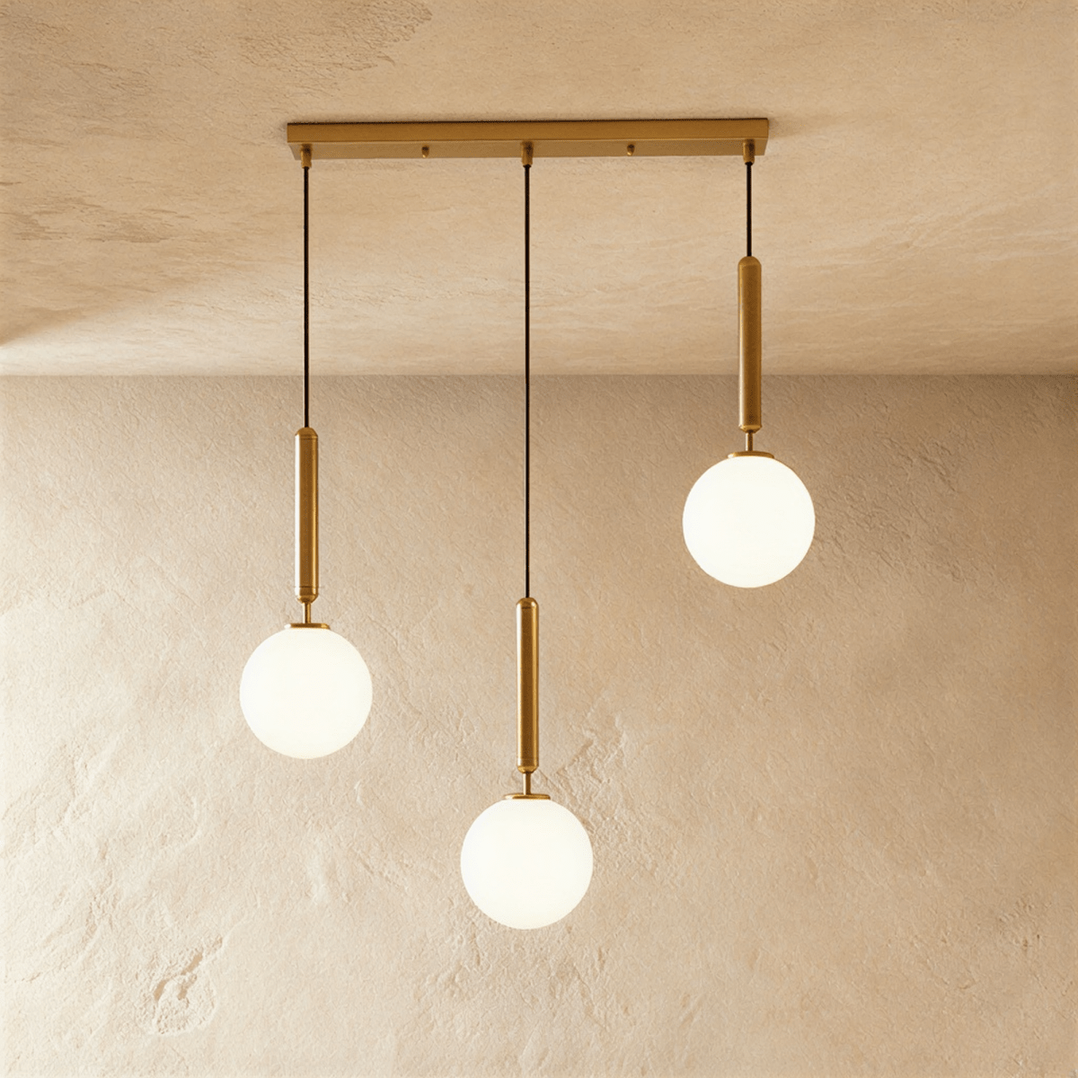 Clérachic three-head linear pendant on a gold bar, with milk white glass globes hung at three different heights.