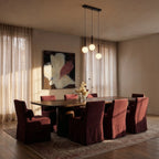 Clérachic linear three-globe pendant in black and milk white, hung over a long dark wood dining table with plum chairs.