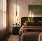 Clérachic single gold pendant with a clear faceted globe glowing beside a bed with a green velvet headboard and nightstand.
