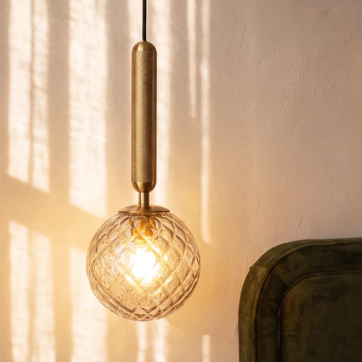 Close view of a Clérachic pendant with a knurled brushed gold rod and a clear diamond-cut glass globe lit by a warm bulb.