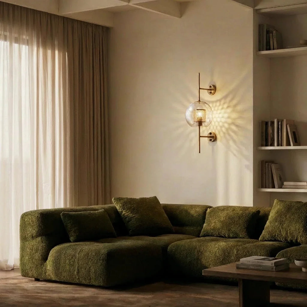 Clérachic wall lamp in its globe shade, lit above a green boucle sectional in a book-lined living room corner.