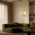 Clérachic wall lamp in its globe shade, lit above a green boucle sectional in a book-lined living room corner.