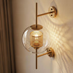 Clérachic wall lamp's globe shade seen close up from a three-quarter angle, its brass cylinder punched with round holes and lit from within behind the clear glass.