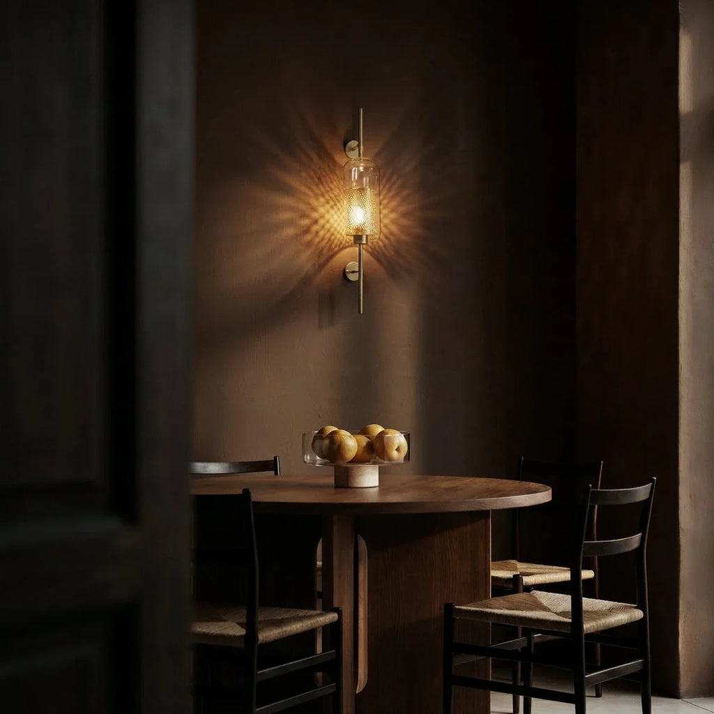 Clérachic wall lamp lit above a round timber dining table set with a bowl of fruit, its dotted pattern radiating across the wall behind.
