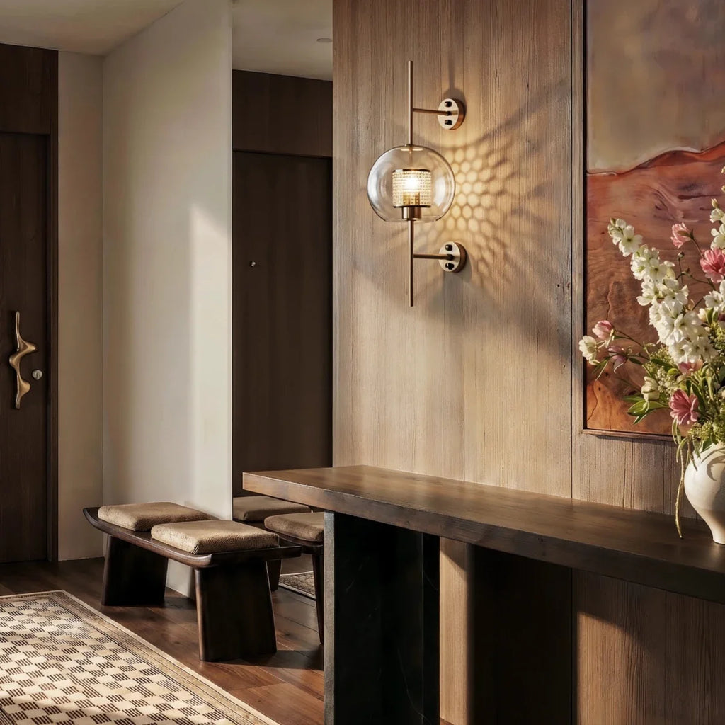 Clérachic wall lamp lit in a wood-panelled entryway, its globe shade glowing beside a console table and a vase of flowers.