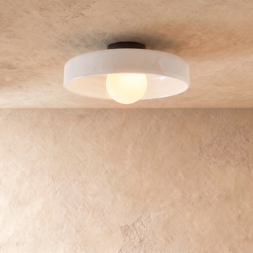 Clérachic shallow white glass disc ceiling light with an opal globe bulb and black canopy, against limewash plaster.