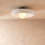 Clérachic shallow white glass disc ceiling light with an opal globe bulb and black canopy, against limewash plaster.