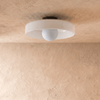 Clérachic shallow white glass disc ceiling light, switched off, showing a pale opal globe bulb and slim black canopy.